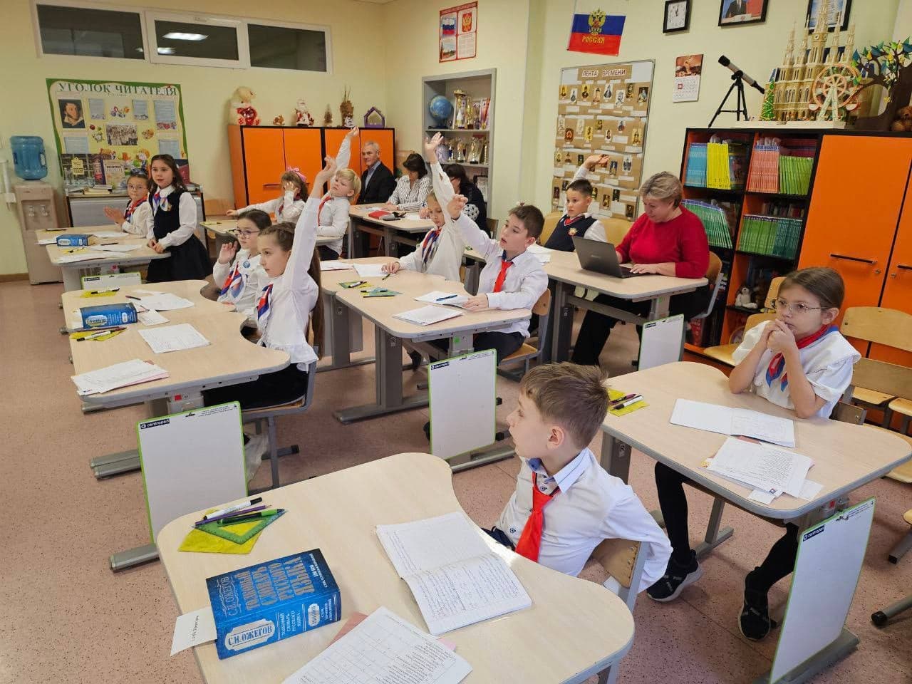 Ученики начального класса поднимают руки на уроке в гимназии